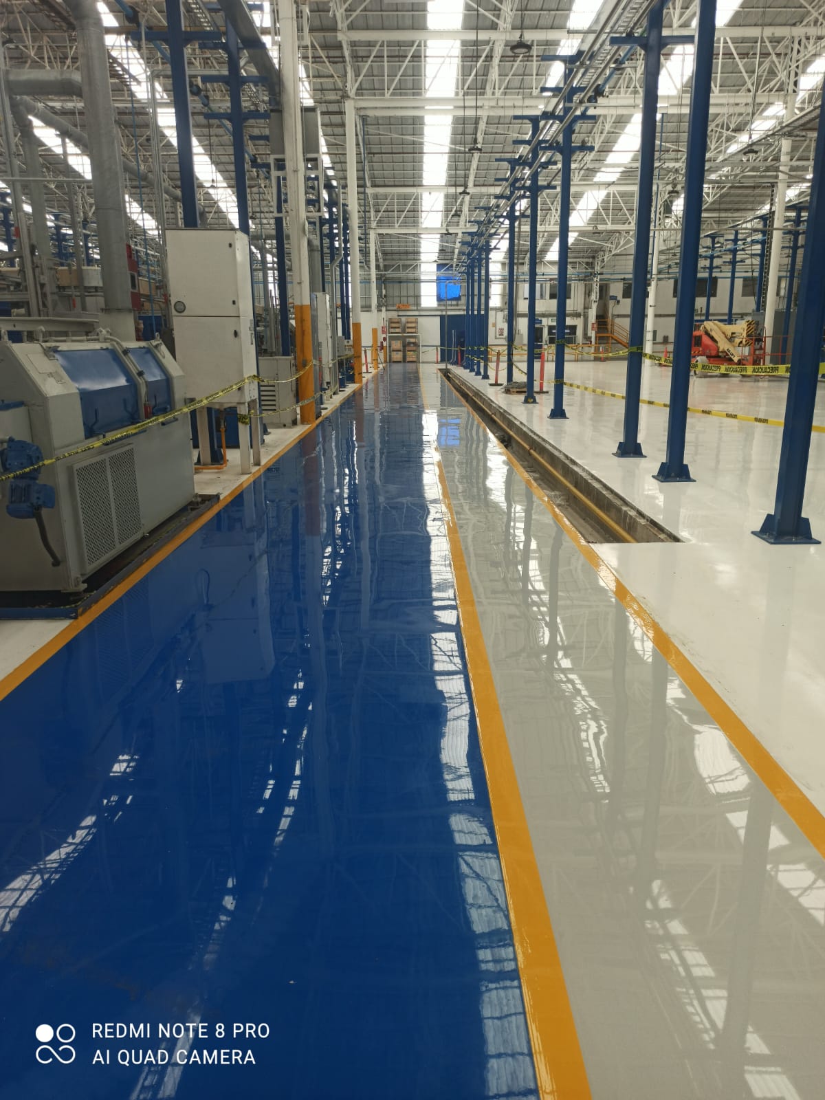 Piso epóxico industrial azul con señalización amarilla aplicado por PEICO